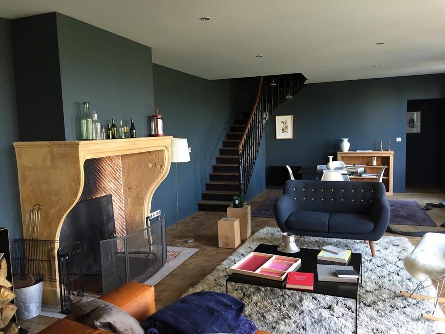 Salon aux murs bleu sombre doté d'une grande cheminée en pierre et d'un escalier en bois à La Tour-du-Pin