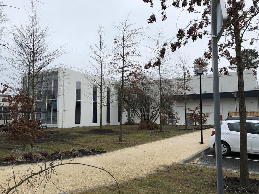 Façade d'un bâtiment moderne blanc aux baies vitrées avec un chemin piéton et des arbres, Merck Biodevelopment à Martillac