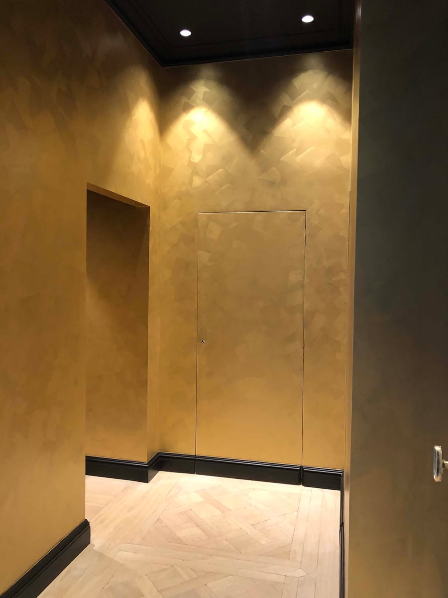 Couloir intérieur aux murs à la peinture dorée texturée et au parquet clair illuminé par des spots, dans un appartement, à Bordeaux