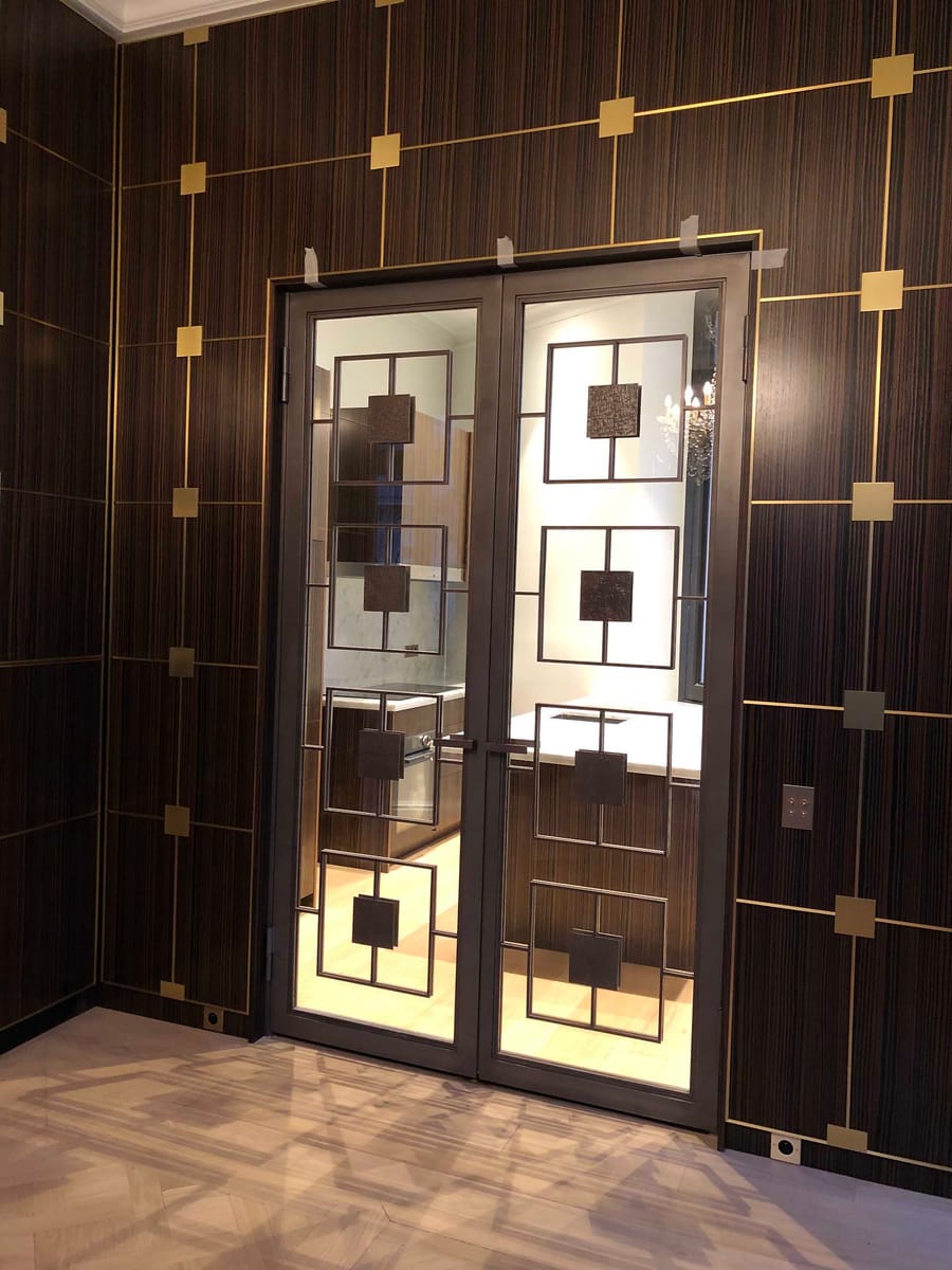 Double porte vitrée à motifs géométriques et mur en bois foncé orné de lignes dorées, dans un appartement, à Bordeaux