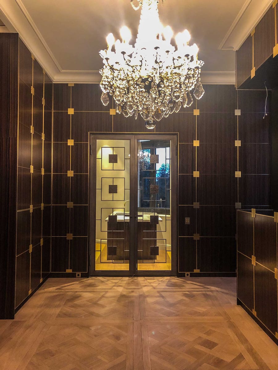 Entrée décorée de boiseries sombres aux détails dorés, avec un lustre en cristal et une porte vitrée géométrique, à Bordeaux