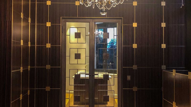 Portes vitrées aux lignes géométriques et murs en bois sombre aux détails dorés dans un appartement, à Bordeaux