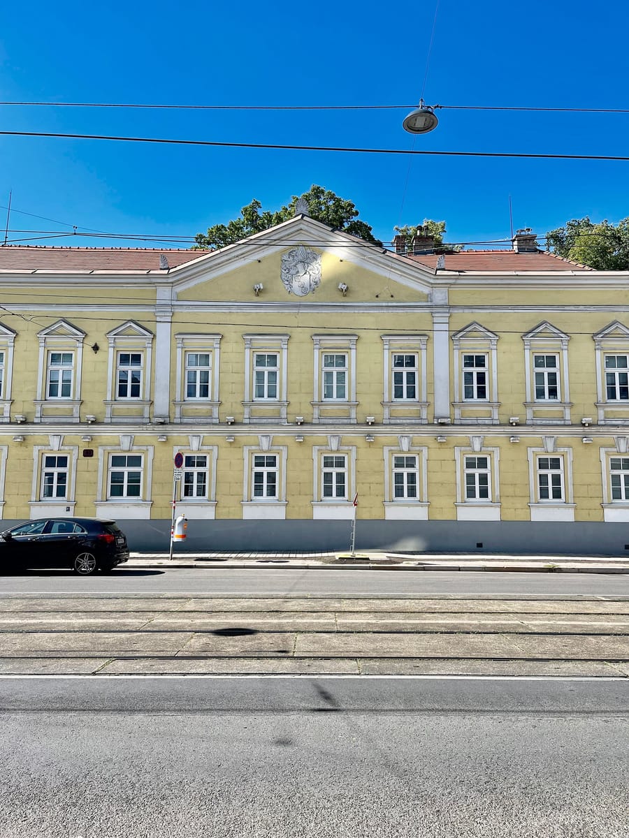 Façade d'un bâtiment classique aux murs jaunes et fronton sculpté, vue depuis une rue avec rails de tramway, Schlumberger en Autriche