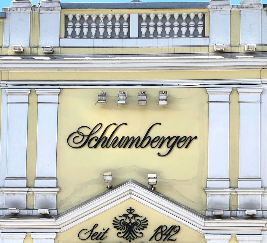 Façade d'un bâtiment néoclassique jaune et blanc arborant l'enseigne Schlumberger sous une balustrade, en Autriche
