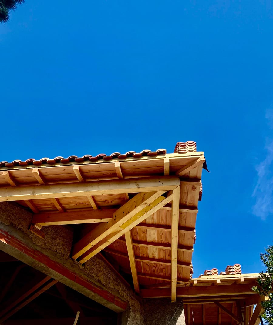 Charpente en bois et toiture en tuiles de terre cuite sous un ciel bleu dégagé sur le chantier de la Villa PND, au Cap Ferret