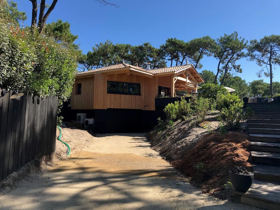 Villa moderne en bardage bois avec toit en tuiles, entourée de pins maritimes au bout d'une allée sableuse, au Cap Ferret