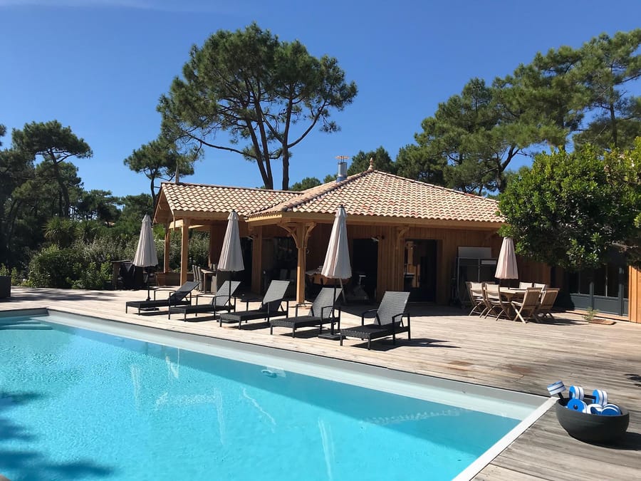 Piscine extérieure bordée d'une terrasse en bois aménagée de transats devant une villa sous les pins, au Cap Ferret