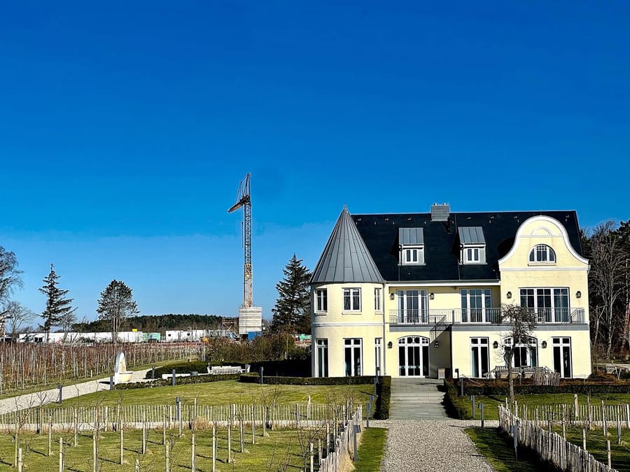 Bâtiment à tourelle aux façades jaunes entouré d'un jardin et de vignes sous un ciel bleu