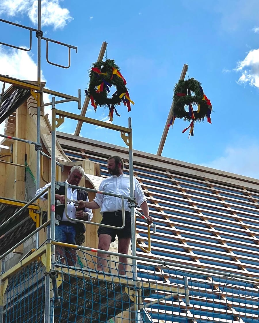 Deux charpentiers sur un échafaudage célébrant la pose d'une charpente en bois ornée de couronnes traditionnelles sur un chantier, Winery Waalem sur l'île de Föhr, en Allemagne