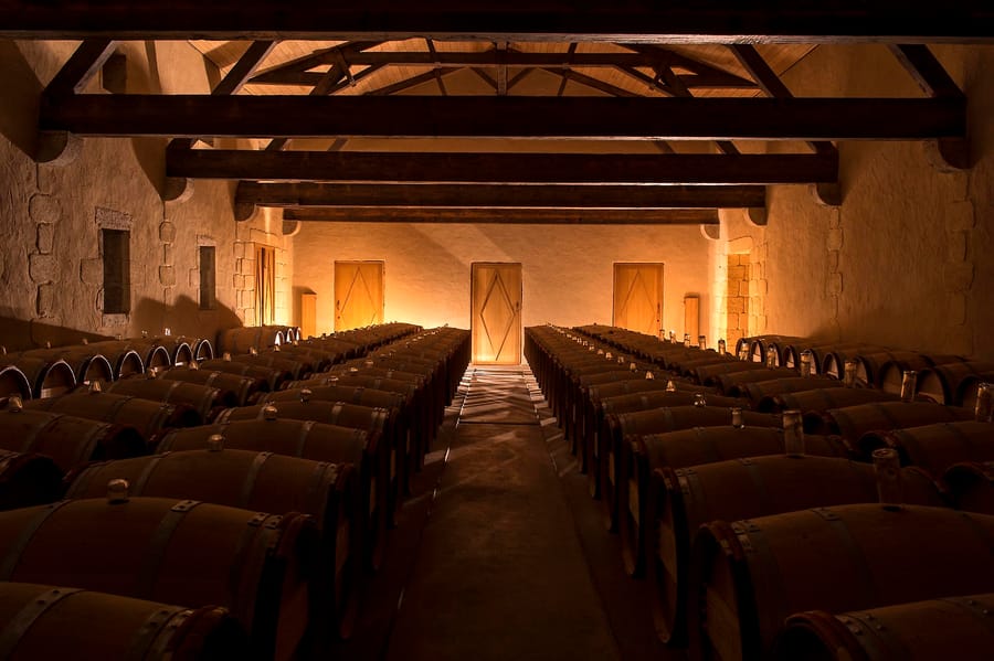 Alignement de barriques de vin en bois sous une charpente apparente dans le chai d'un domaine viticole, Château d'Yquem à Sauternes