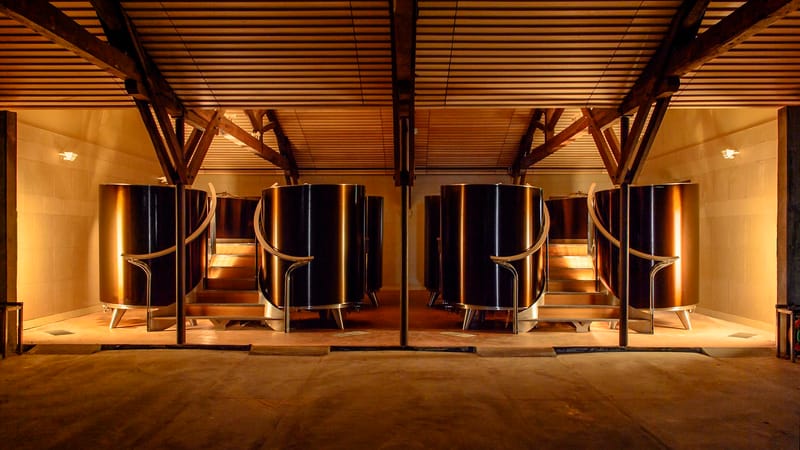 Cuves vinicoles métalliques et escaliers en bois installés sous une charpente éclairée dans un chai moderne, Château d'Yquem à Sauternes