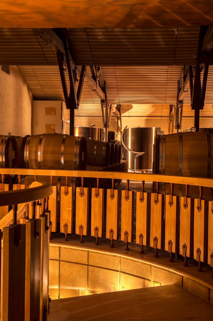 Fûts de chêne et cuves en inox dans un chai viticole à l'architecture en bois éclairée, Château d'Yquem à Sauternes