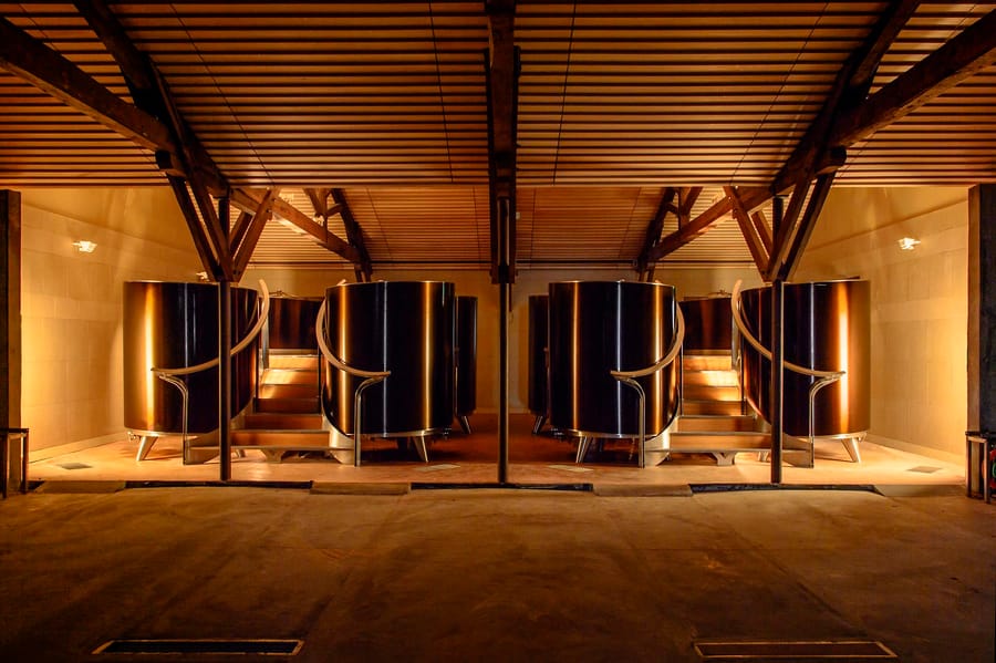 Grandes cuves en inox sous une charpente en bois éclairée dans un chai vinicole, Château d'Yquem à Sauternes