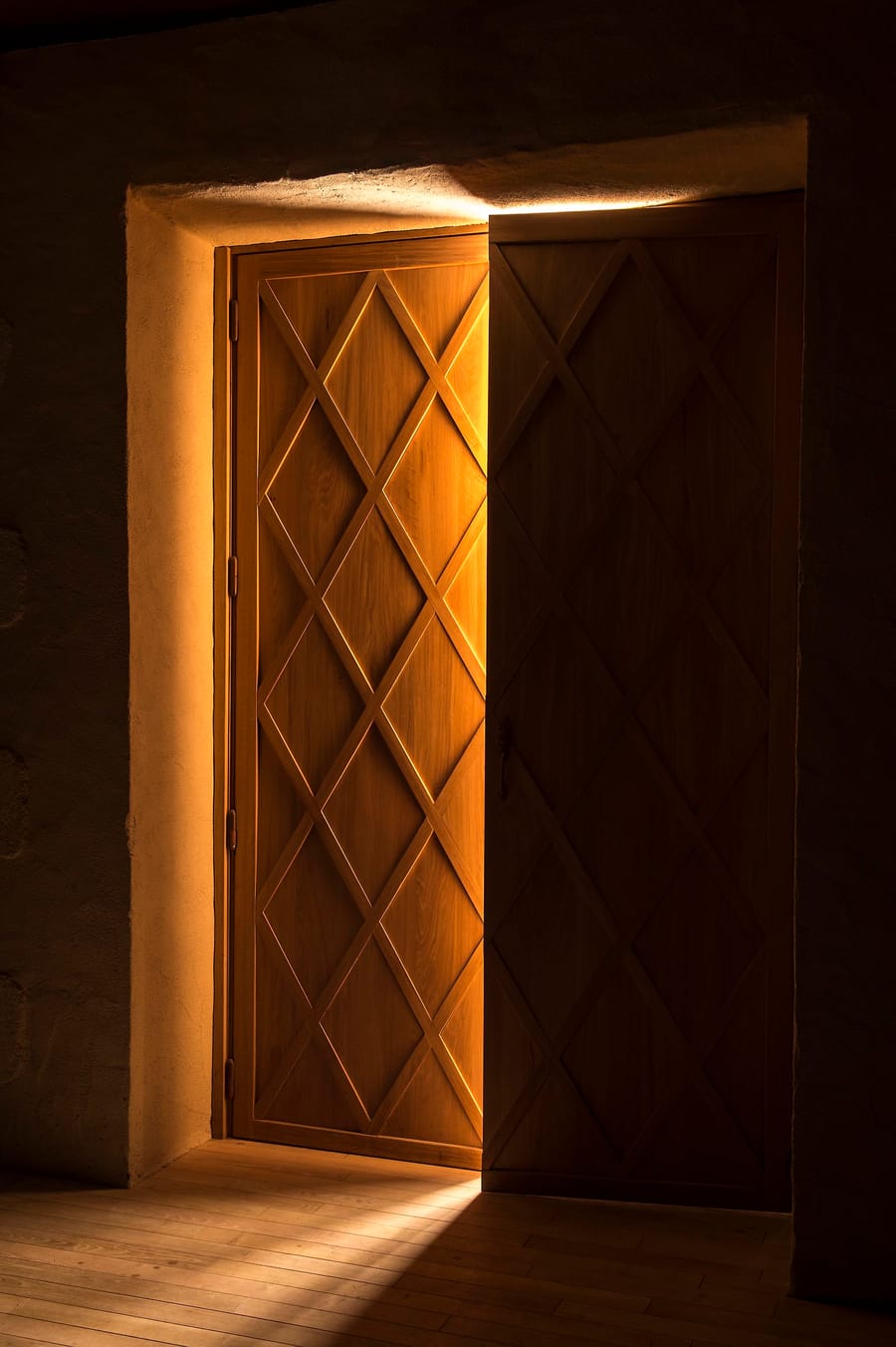 Porte en bois à motifs de losanges entrouverte laissant passer une lumière chaude sur le parquet des chais d'un domaine, Château d'Yquem à Sauternes
