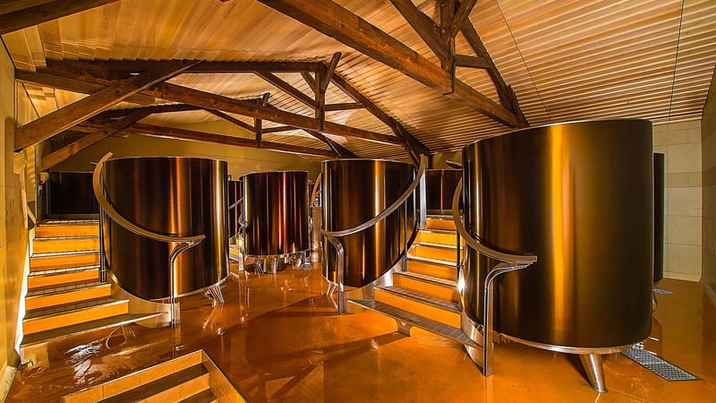 Cuves vinicoles en inox aux reflets dorés sous une charpente en bois, dans un cuvier moderne, Château d'Yquem à Sauternes