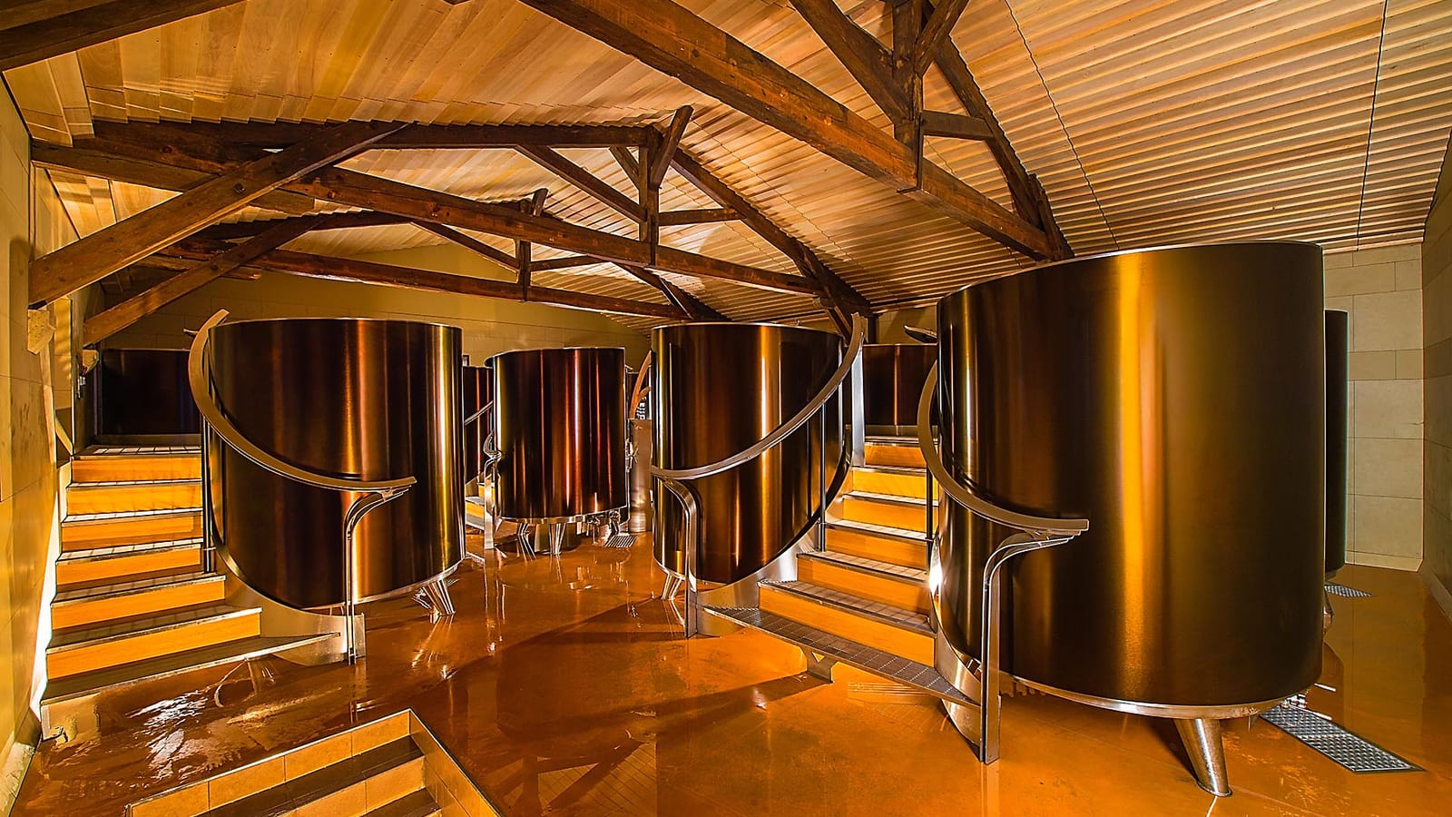 Cuves vinicoles en inox aux reflets dorés sous une charpente en bois, dans un cuvier moderne, Château d'Yquem à Sauternes