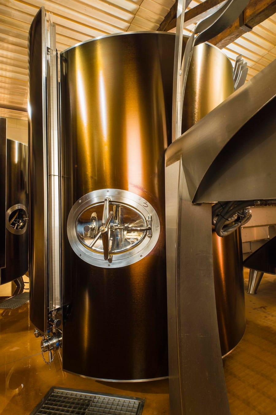 Grande cuve métallique aux reflets cuivrés et trappe en inox installée dans un cuvier viticole, Château d'Yquem à Sauternes