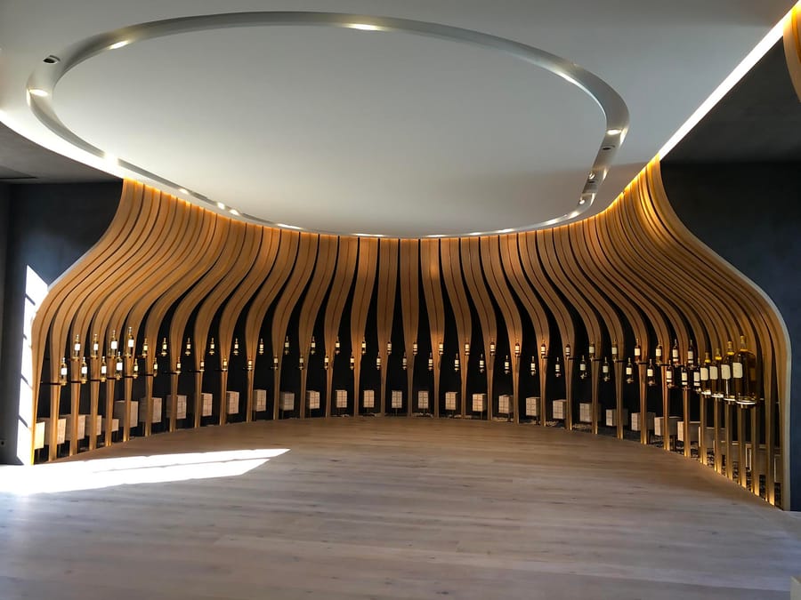 Salle de dégustation contemporaine dotée d'une structure en lattes de bois ondulées exposant des bouteilles de vin, Château d'Yquem à Sauternes