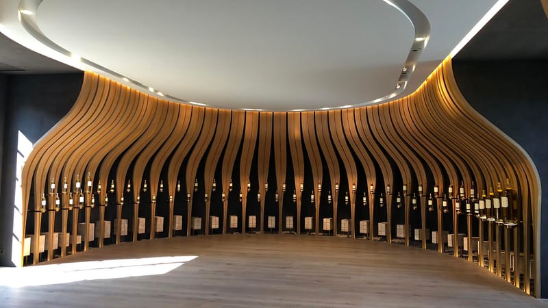 Salle de dégustation contemporaine habillée d'une structure en bois ondulé exposant des bouteilles de vin, Château d'Yquem à Sauternes