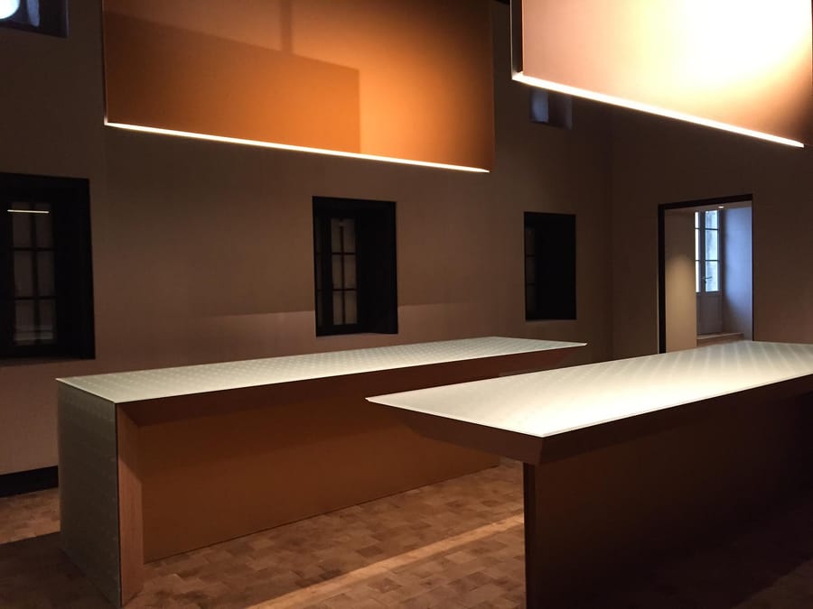Tables de dégustation éclairées sous de grands luminaires suspendus dans une salle au design épuré, Château d'Yquem à Sauternes